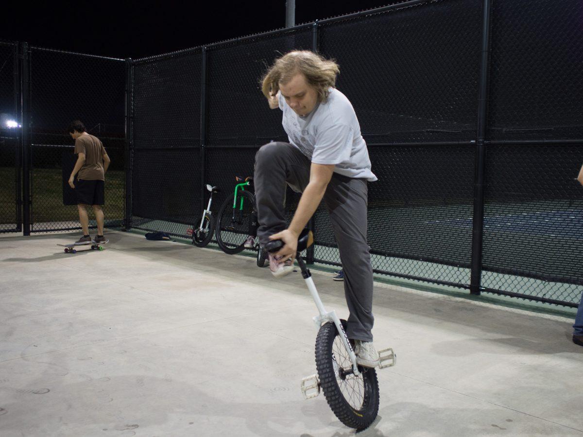 Lee Price, an emerging media and communications senior, practices unicycling at UTD's tennis courts. Price, who serves as the president of UTD's Unicycle Club, picked up the activity while in middle school. Photo by Roman Soriano | Mercury Staff.