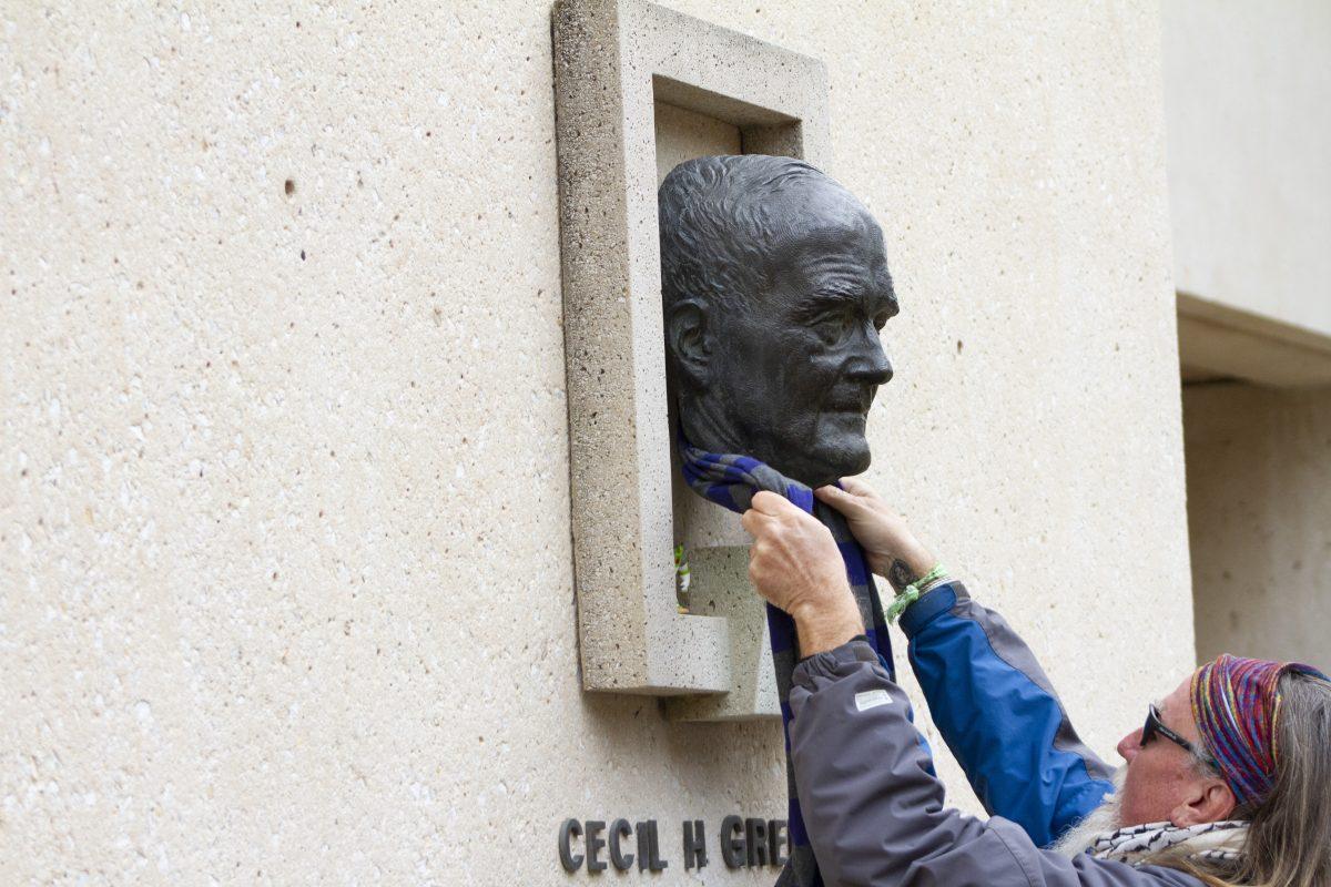 Virgil, who often leaves small toys around campus, drapes a scarf around the bust of Cecil H. Green. Photo by Megan Zerez | Mercury Staff.
