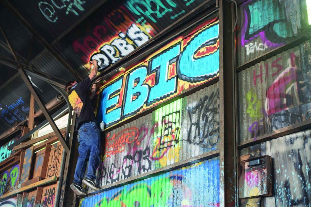 An artist spray paints a design on the ceiling of the Fabrication Yard building, a structure in West Dallas that is open to the public and serves as a safe space for artists and creatives to gather.  Photo by Cindy Folefack | Mercury Staff