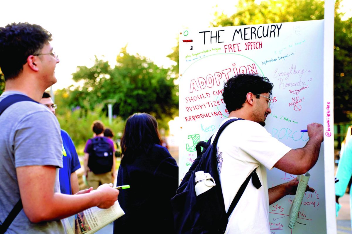 Students pause to share their thoughts on The Mercury’s Free Speech Wall taking turns writing and reading what others have posted. 
